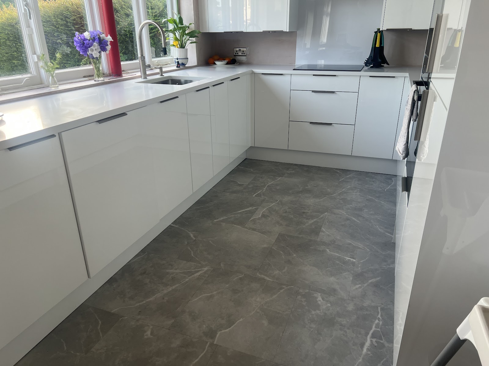 Grey stone-effect flooring laid through a white gloss kitchen, cut cleanly around every unit.